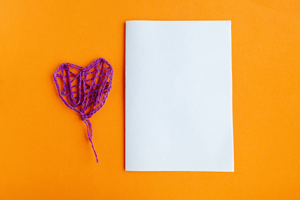 Purple thread handmade heart and white mockup blank on bright orange background, copy space for the text - Foto, afbeelding