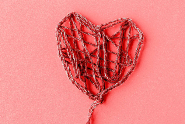 Červená nit ručně vyrobené srdce na růžovém pozadí - Fotografie, Obrázek