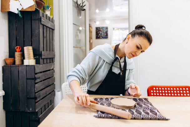 Vrouw rolt klei om een bord te maken in een aardewerk werkplaats - Foto, afbeelding