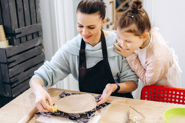 Matka a dcera zdobí hliněný talíř před pálením v keramickém studiu, zdobí talíř s levandulovými větvemi - Fotografie, Obrázek
