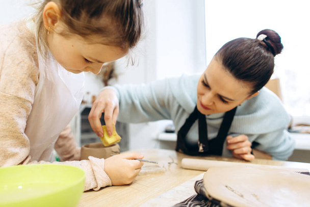 Mother and daughter decorate a clay plate before firing in a pottery studio, decorate a plate with lavender branches - Photo, Image