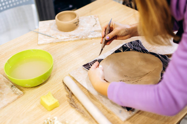 Γυναίκα ετοιμάζει ένα πήλινο πιάτο για ψήσιμο σε ένα στούντιο κεραμικής, διακοσμεί ένα πιάτο με κλαδιά λεβάντας - Φωτογραφία, εικόνα