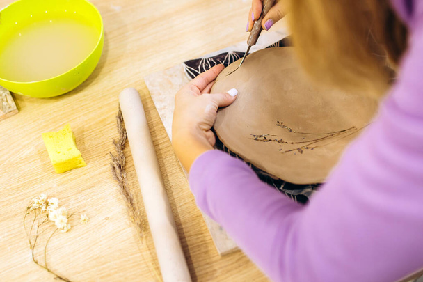 Mujer prepara un plato de arcilla para la cocción en un estudio de cerámica, decora un plato con ramas de lavanda - Foto, Imagen