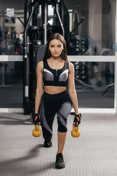 Stretching with weights in the gym a brunette girl is losing weight in a comfortable tight suit. The concept of sport and the power of the spirit. - Fotó, kép
