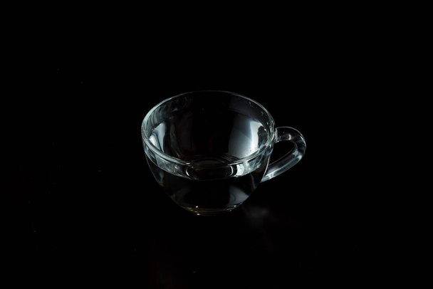 copo de vidro transparente com água em um fundo escuro. Beba em uma xícara na mesa. álcool. saciar a sede. - Foto, Imagem