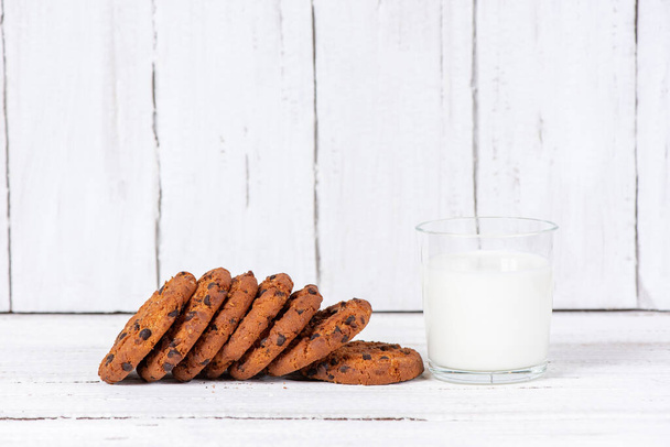 Πεντανόστιμα σπιτικά μπισκότα με σοκολάτα και ένα ποτήρι γάλα σε ξύλινο λευκό τραπέζι. Όμορφη νεκρή ζωή  - Φωτογραφία, εικόνα