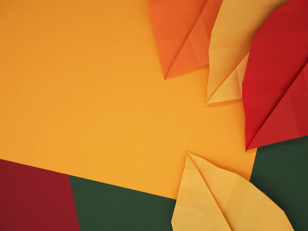 Hojas de origami de papel sobre fondo de papel temático de otoño en amarillo, verde y rojo - Foto, imagen