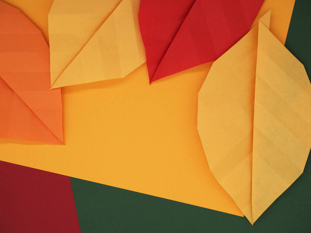 Paper origami leaves on autumn themed paper background in yellow, green, and red - Fotoğraf, Görsel