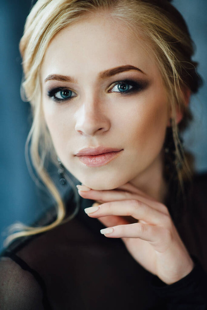 Blondes Mädchen mit blauen Augen in einem schwarzen Kleid im dunkeltürkisfarbenen Interieur - Foto, Bild