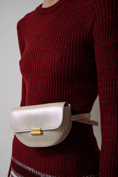 Slim girl in red sweater with leather pearl handbag. White fashionable luxury waist bag. Vertical photo. - Foto, Imagen