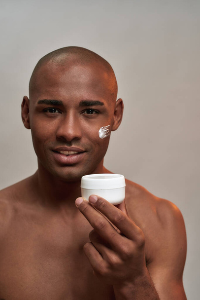 Cosmetics jar held by multiracial male with cream on face - Foto, imagen