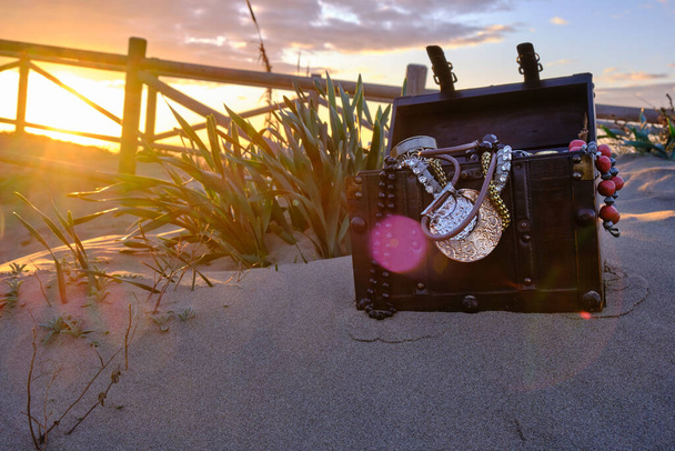 baú do tesouro na praia em um nascer do sol, jóias e moedas de ouro - Foto, Imagem