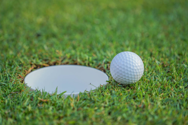 A bola no buraco do campo de golfe. Bola de golfe colocando na grama verde perto de buraco de golfe para ganhar no jogo no campo de golfe com fundo borrão.                                - Foto, Imagem