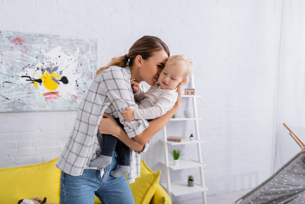 joven mujer sosteniendo y abrazando a su hijo pequeño en casa - Foto, Imagen