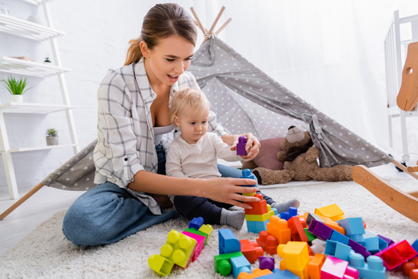 молода мати грає з будівельними блоками з сином на підлозі біля дітей вігвам
 - Фото, зображення