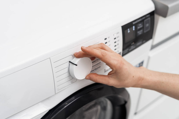 Cropped view of woman choosing delicate cycle or select program at modern automatic washing machine. Housewife regulate settings, turning knob on control panel. Laundry and housework concept - Photo, Image