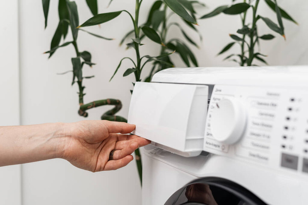 Обрізаний вид жіночої контейнер для відкриття рук для прання порошку або пом'якшувача на автоматичній пральній машині. Концепція прання та побутового обладнання у ванній
 - Фото, зображення