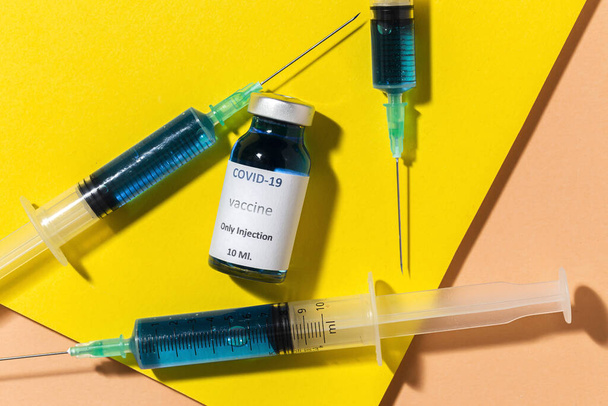 Transparent glass vials with test COVID-19 vaccine, with syringes on colorful background from above.Flat lay - 写真・画像