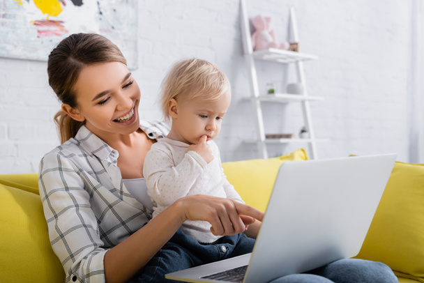 smiling freelancer pointing at laptop while holding little son - Φωτογραφία, εικόνα