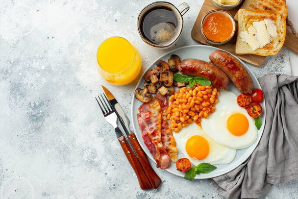 Повний англійський сніданок на тарілці з смаженими яйцями, ковбасою, беконом, бобами, тостами і кавою на легкому кам'яному фоні. Простір копіювання. Краєвид. - Фото, зображення