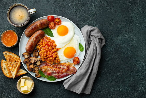 Повний англійський сніданок на тарілці з смаженими яйцями, ковбасою, беконом, бобами, тостами і кавою на темному кам'яному тлі. Простір копіювання. Краєвид. - Фото, зображення