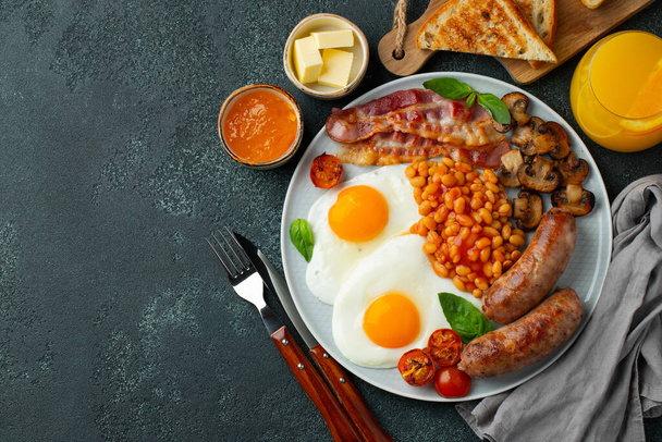 Повний англійський сніданок на тарілці з смаженими яйцями, ковбасою, беконом, бобами, тостами і кавою на темному кам'яному тлі. Простір копіювання. Краєвид. - Фото, зображення