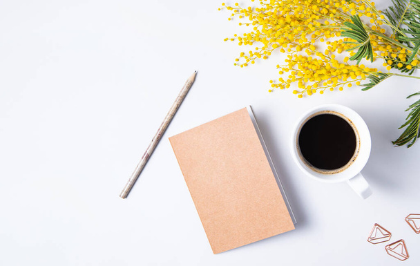 Flat lay com flor de mimosa amarela, xícara de café, caderno de artesanato e lápis em uma mesa de mármore. desktop floral das mulheres. Conceito da manhã de primavera. vista superior e espaço de cópia - Foto, Imagem