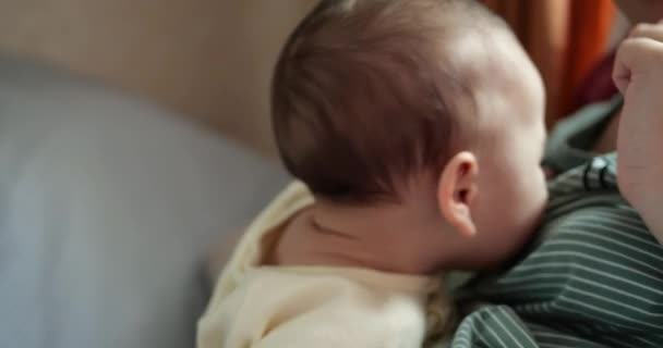 una giovane madre sta tenendo un bellissimo figlio di sette mesi che sorride e rode le dita e le madri mano. prurito ai denti di un neonato, dentizione - Filmati, video