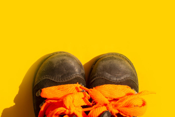 zapatos infantiles desgastados con cordones naranjas sobre un fondo amarillo. - Foto, imagen