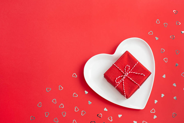 Мала червона подарункова коробка на білій пластині у формі серця
. - Фото, зображення