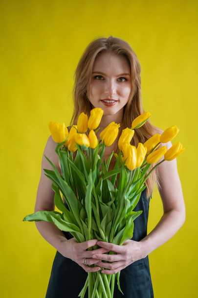 Caucasian woman with an armful of yellow tulips on a yellow background. International Womens Day. Bouquet of spring flowers - Zdjęcie, obraz