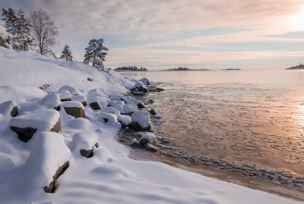 costa de hielo en el agua en el lago Ladoga al amanecer con nieve fresca en la puesta de sol de invierno - Foto, Imagen