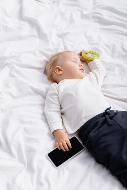 Hochblickbild des schlafenden Kindes mit Rassel und Smartphone mit leerem Bildschirm zu Hause - Foto, Bild