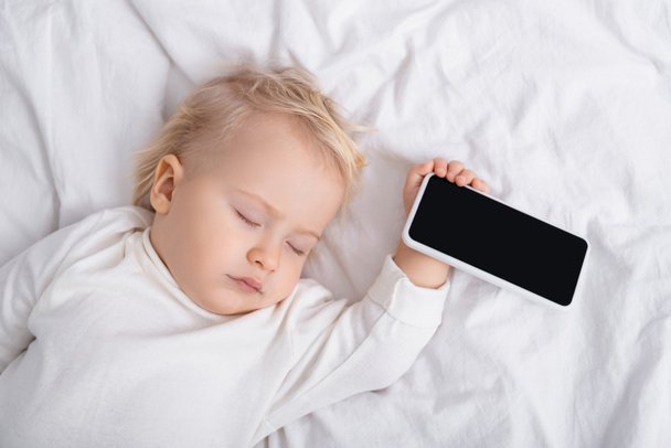 Beyaz ekranlı akıllı telefonun yanında uyuyan bebeğin üst görüntüsü. - Fotoğraf, Görsel