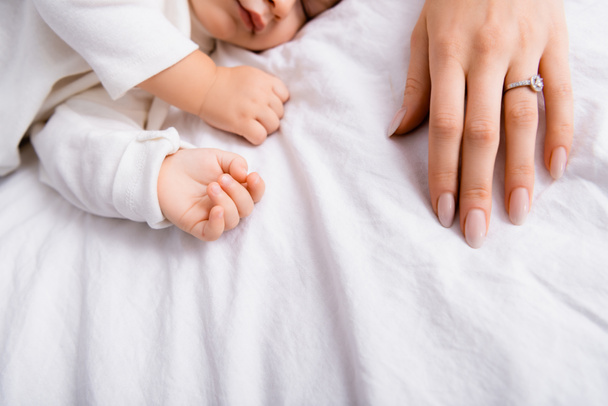 mothers hand near little son sleeping on white bedding, cropped view - Photo, Image