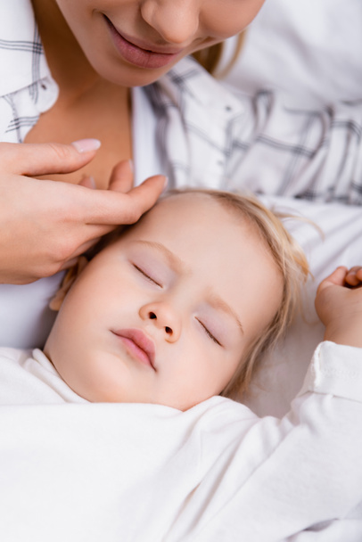 Gülümseyen kadın, uyuyan küçük çocuğun kafasına dokunuyor. - Fotoğraf, Görsel