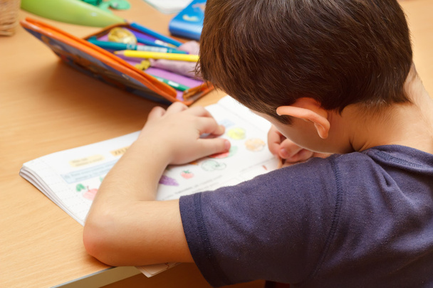 Menino fazendo lição de casa com lápis de cor, pintando frutas
 - Foto, Imagem
