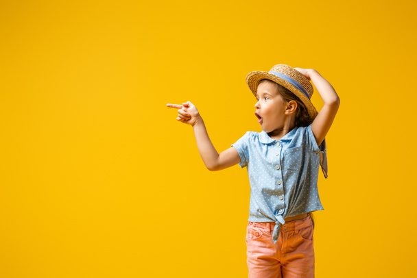 wstrząśnięty dzieciak w słomkowym kapeluszu wskazując palcem na żółto - Zdjęcie, obraz