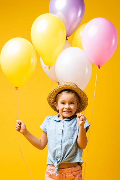 happy kid in straw hat holding balloons isolated on yellow - Photo, Image
