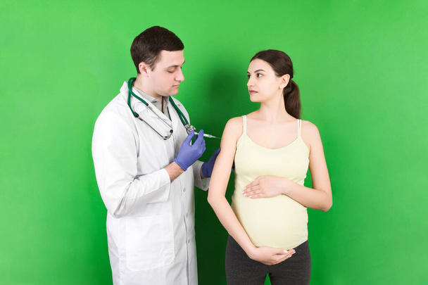Neugeborenes Familienkonzept. Eine schwangere Frau mit der Hand eines Arztes, um zu impfen, eine Krankenschwester, die ein junges Mädchen impft, das ein Kind hat oder sich in der Gebärmutter entwickelt. - Foto, Bild