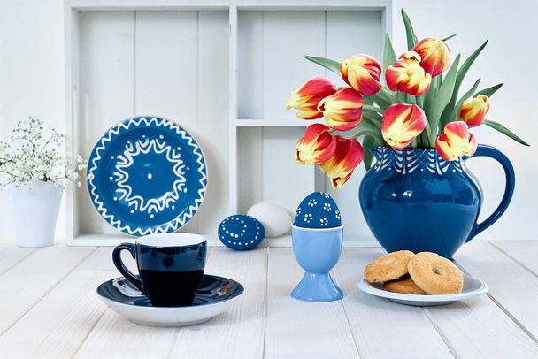 Cup of coffee and cookies on off white table. Bunch of pussy-willow in blue ceramic jar and matching springtime decorations. Eco friendly zero waste Easter. Rustic casual spring coffee time setup. - Φωτογραφία, εικόνα