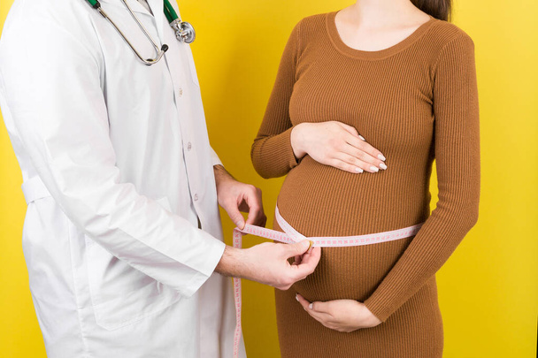 gelukkig mooi zwanger jong vrouw aanraken van haar blote buik terwijl een arts is het meten. - Foto, afbeelding