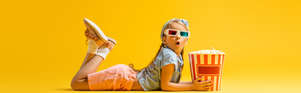 sokkos lány 3D-s szemüvegben feküdt közel popcorn vödör sárga, banner - Fotó, kép