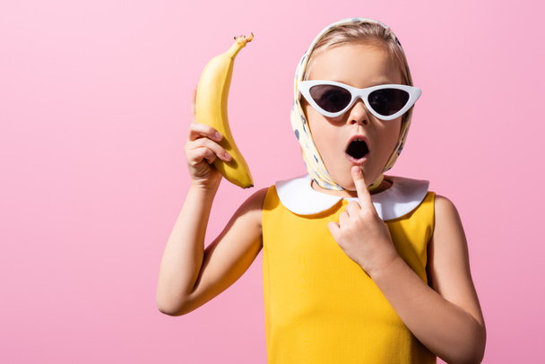 shocked girl in headscarf and sunglasses holding banana isolated on pink - Photo, Image