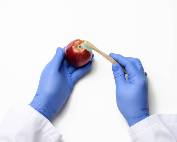 Hand in blauem Latex-Handschuh hält einen reifen roten Apfel auf weißem Hintergrund, Draufsicht - Foto, Bild