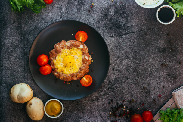 Beefsteak with egg on a plate. Delicious hot dish. The dish is decorated with cherry tomatoes and herbs. Beefsteak on a plate  - Фото, зображення