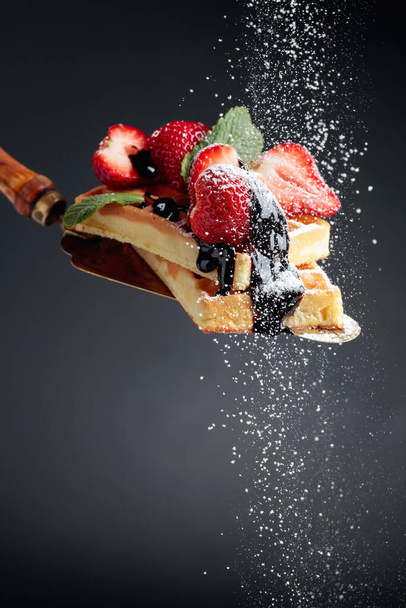 Waffles with strawberries, mint and chocolate sauce, sprinkled with powdered sugar. - Photo, Image