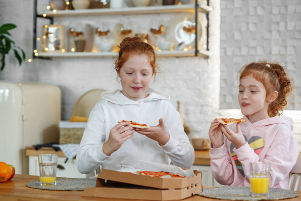 Молоді дівчата з рудим волоссям на кухні їдять піцу, п'ють сік. Зустрічі з подружками, дві сестри
. - Фото, зображення