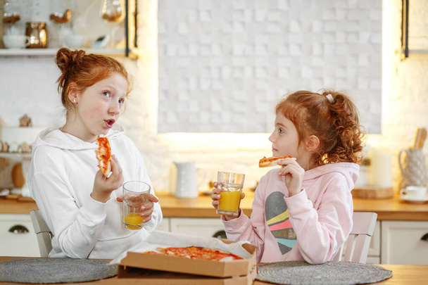 Young girls with red hair in the kitchen eating pizza, drinking juice. Get-togethers with girlfriends, two sisters. - Foto, Imagem