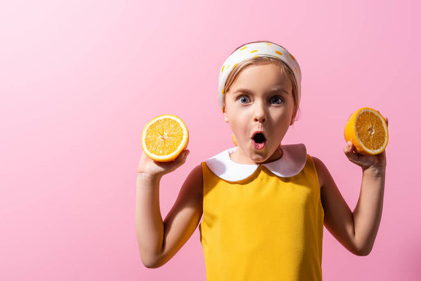 shocked girl in headscarf holding orange halves isolated on pink  - Fotó, kép